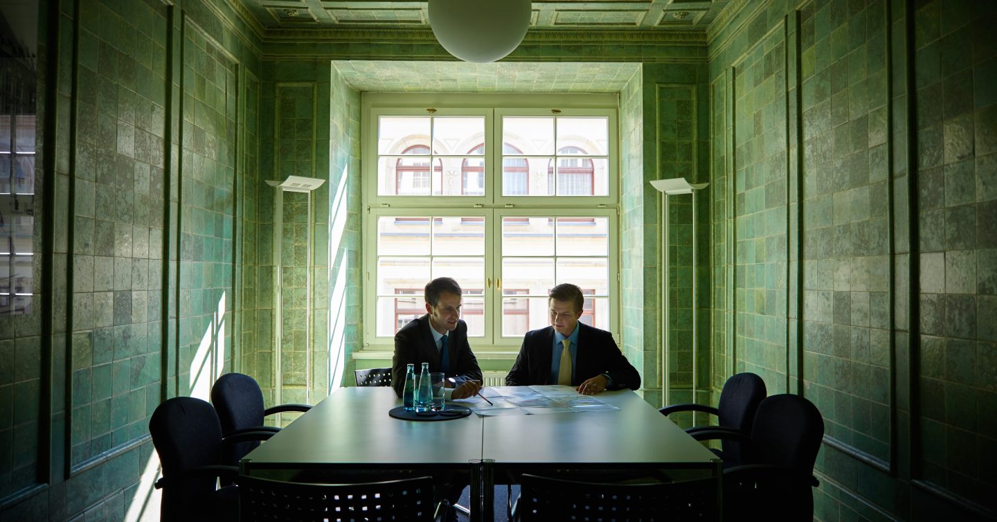Zwei Berater besprechen einen Plan in einem Besprechungsraum mit grün gefliesten Wänden