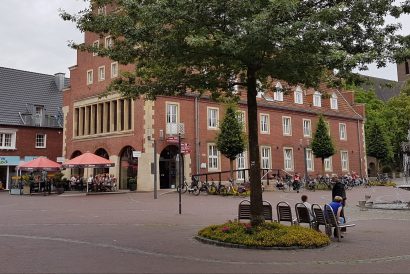 Marktplatz in Vreden mit Backsteinbauten, Brunnen, Bänken und Außengastronomie