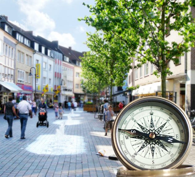 Fußgängerzone mit Wasserspiel und Passanten, im Vordergrund ein Kompass