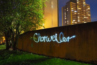 Lichtgraffiti mit dem Schriftzug Chorweiler vor beleuchteten Hochhäusern bei Nacht