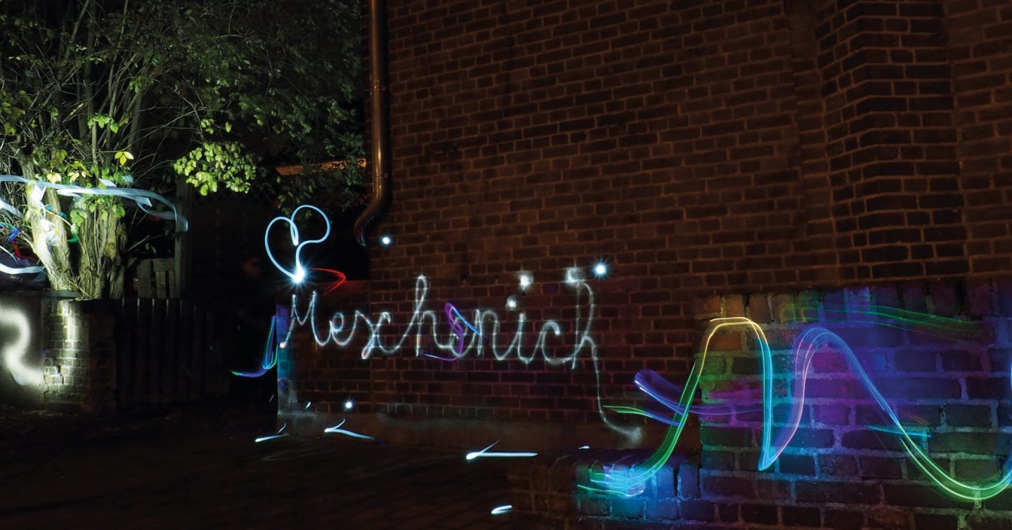 Lichtgraffiti mit dem Schriftzug Meschenich an einer Backsteinmauer bei Nacht