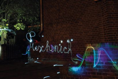 Lichtgraffiti mit dem Schriftzug Meschenich an einer Backsteinmauer bei Nacht