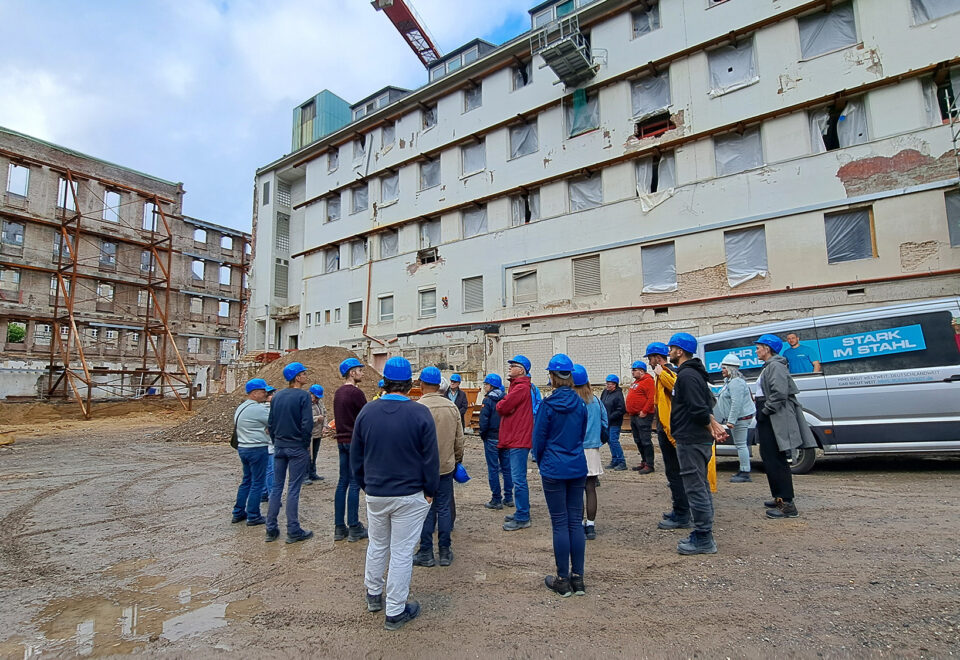 Gruppe mit blauen Schutzhelmen bei einer Begehung vor einem Gebäude im Umbau