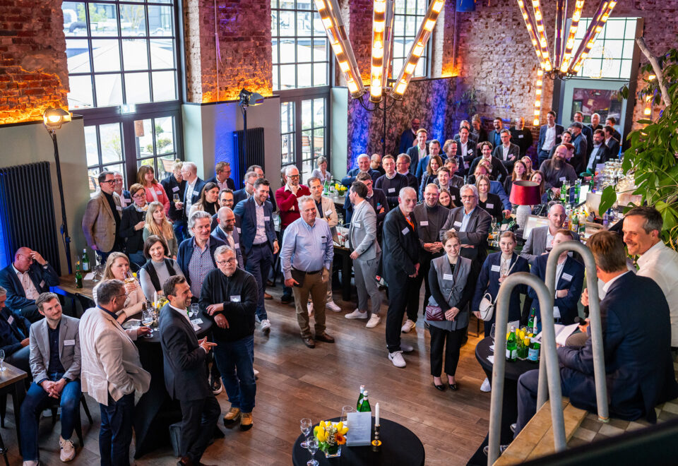 Gäste einer Abendveranstaltung verfolgen ein Gespräch in einer Halle mit Backsteinwänden